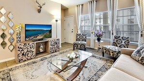A living room with a television, patterned chairs, a glass coffee table, and a decorative mirror. - Lake View - Gorgeous Lake Travis Island Condo!!! (Lago Vista)