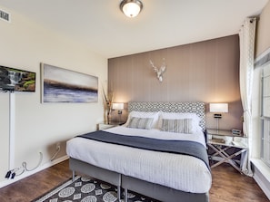 Una habitación de hotel moderna con una cama grande, dos mesitas de noche, un televisor montado y una pieza decorativa en la pared.