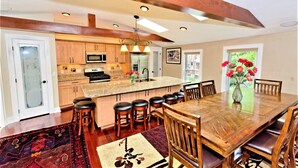 A spacious kitchen with wooden cabinets, a central island with stools, and a dining area with a wooden table and chairs.