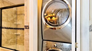 A modern laundry room with two front-loading washing machines, a glass shower enclosure, and a tiled floor.