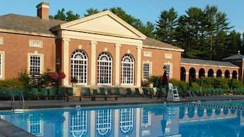 Stunning facade with arched windows and a central pediment, adjacent to a serene pool area with lounge chairs and a small bridge.