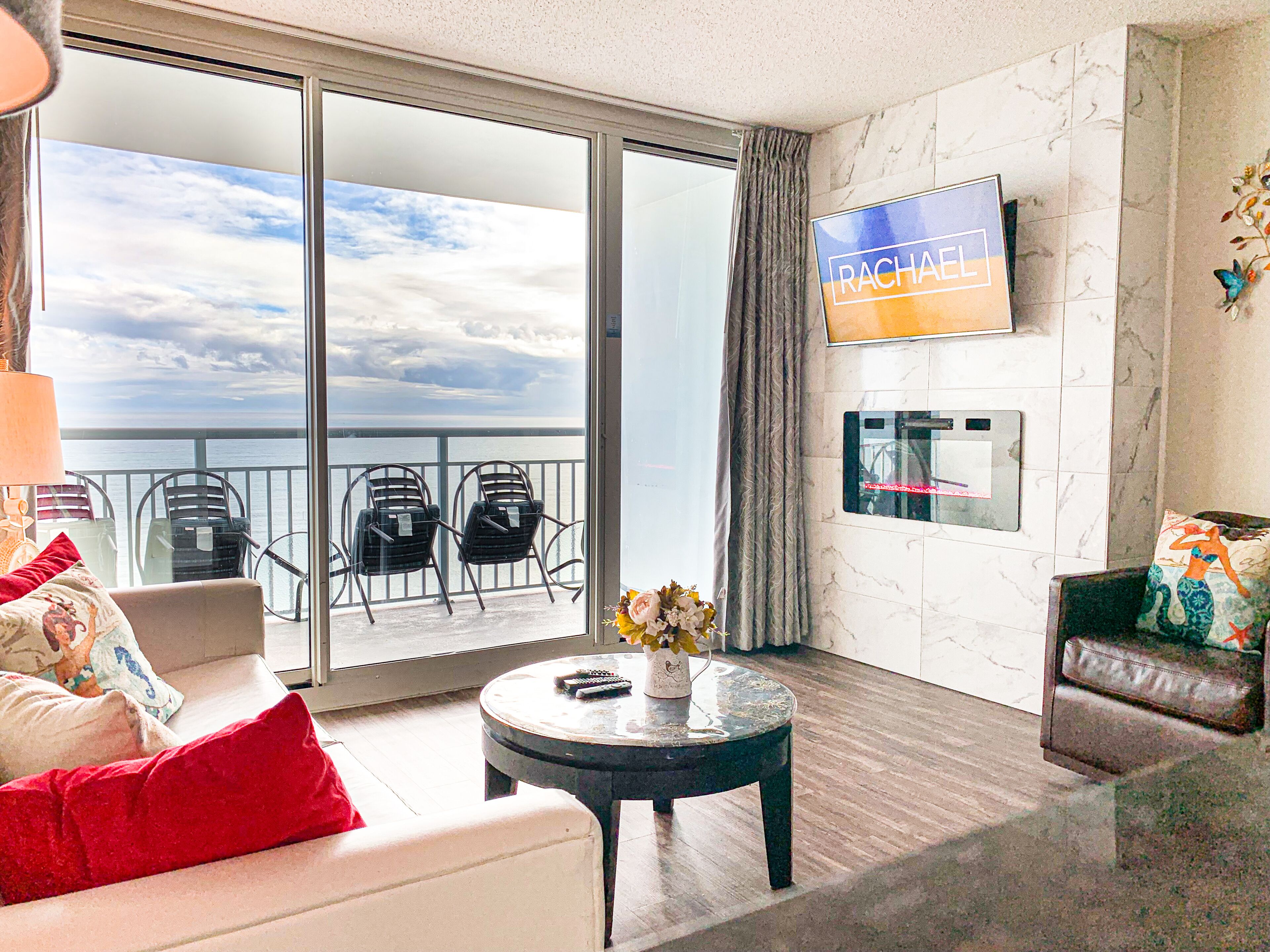 A modern hotel room with a balcony, a flat-screen TV, a coffee table, and a sofa.