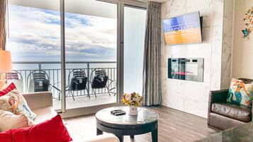 A modern hotel room with a balcony, a flat-screen TV, a coffee table, and a sofa.