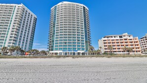 Un hôtel situé en bord de mer, avec plusieurs étages, des balcons et une vue dégagée sur l’océan.