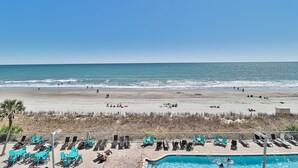 Une vue sur la plage avec une piscine, des chaises longues et un ciel dégagé.
