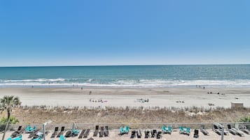 Vista de una playa con zona de piscina, sillas de descanso y cielo despejado.