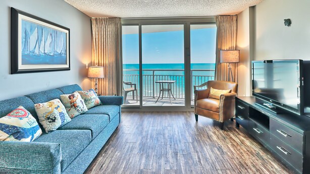Une chambre d’hôtel avec un balcon, un canapé, un fauteuil, une télévision et un tableau.