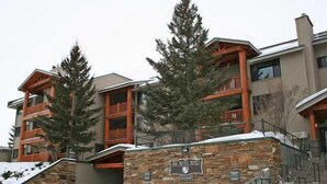 A multi-story hotel with stone and wood exterior, balconies, and a stone entrance with stairs. - TRUE SKI IN/SKI OUT, SLOPESIDE 3 BR CONDO - PATIO, HOT TUB, POOL, FREE PARKING (Park City)