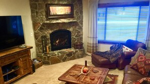 A living room with a stone fireplace, leather sofas, a coffee table, and a flat-screen TV. - TRUE SKI IN/SKI OUT, SLOPESIDE 3 BR CONDO - PATIO, HOT TUB, POOL, FREE PARKING (Park City)