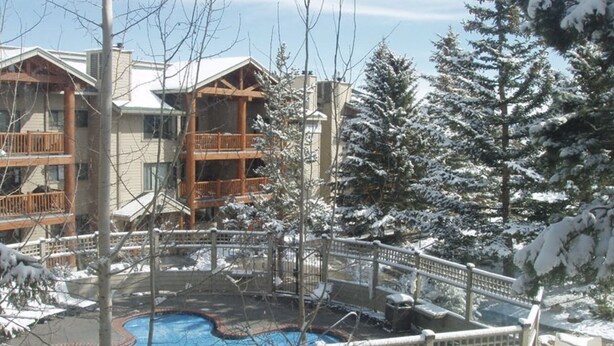 A resort with a pool, wooden balconies, and snow-covered trees. - TRUE SKI IN/SKI OUT, SLOPESIDE 3 BR CONDO - PATIO, HOT TUB, POOL, FREE PARKING (Park City)