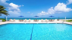 A clear blue pool with lounge chairs and umbrellas, overlooking the ocean.