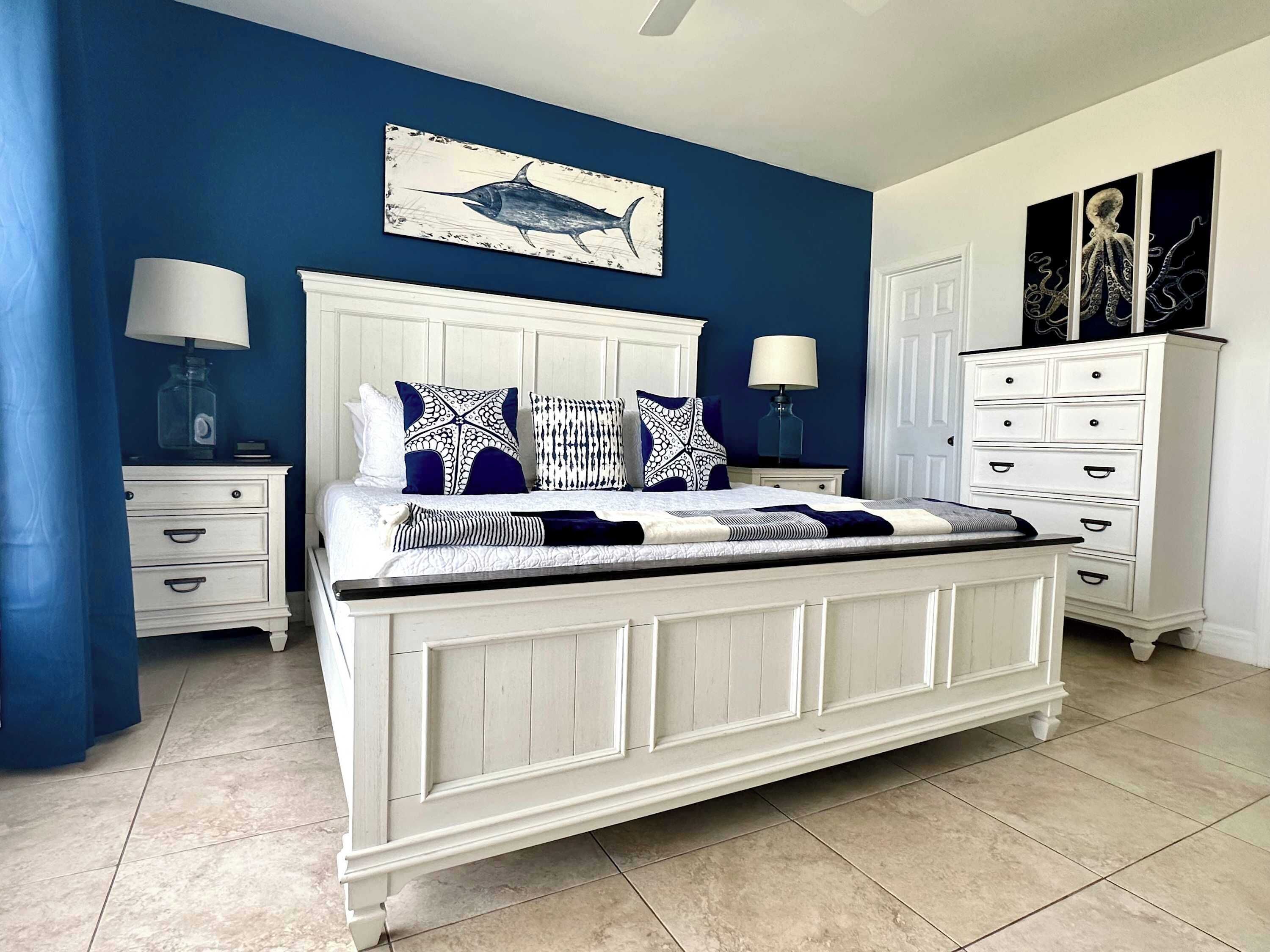 Quarto com uma cama grande, mesas de cabeceira brancas, cômoda e uma parede com pintura de tubarão.