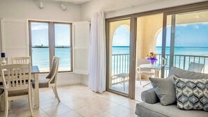 A balcony with a view of the sea, a dining area with a table and chairs, and a sofa with patterned cushions.