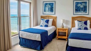A hotel room with two beds, a view of the sea, and two framed pictures of palm trees.