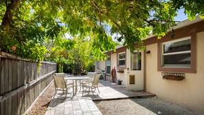 A patio with a table and chairs, a wooden fence, and a house with a door and windows. - Vanderbilt Beach (Naples)
