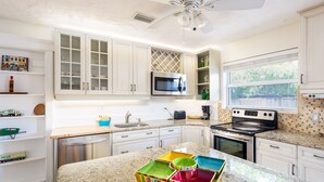 A kitchen with white cabinets, a microwave, a stove, and colorful storage containers on the countertop. - Vanderbilt Beach (Naples)