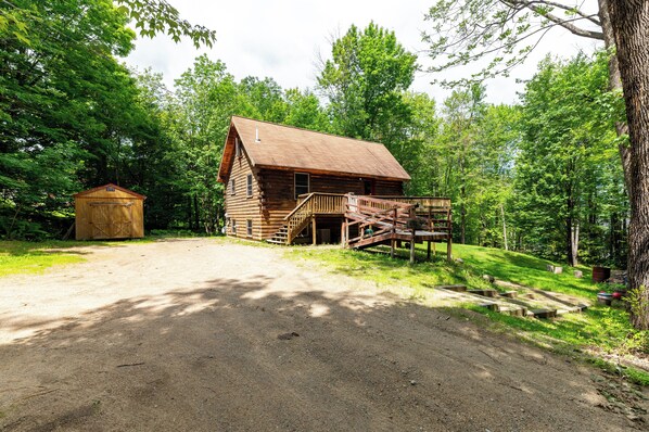 A rustic log cabin with a wooden deck and a small shed nearby.