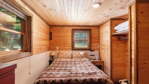 Ein Schlafzimmer einer Holzhütte mit einem Bett, einem Nachttisch, einem Fenster und einer Tür.