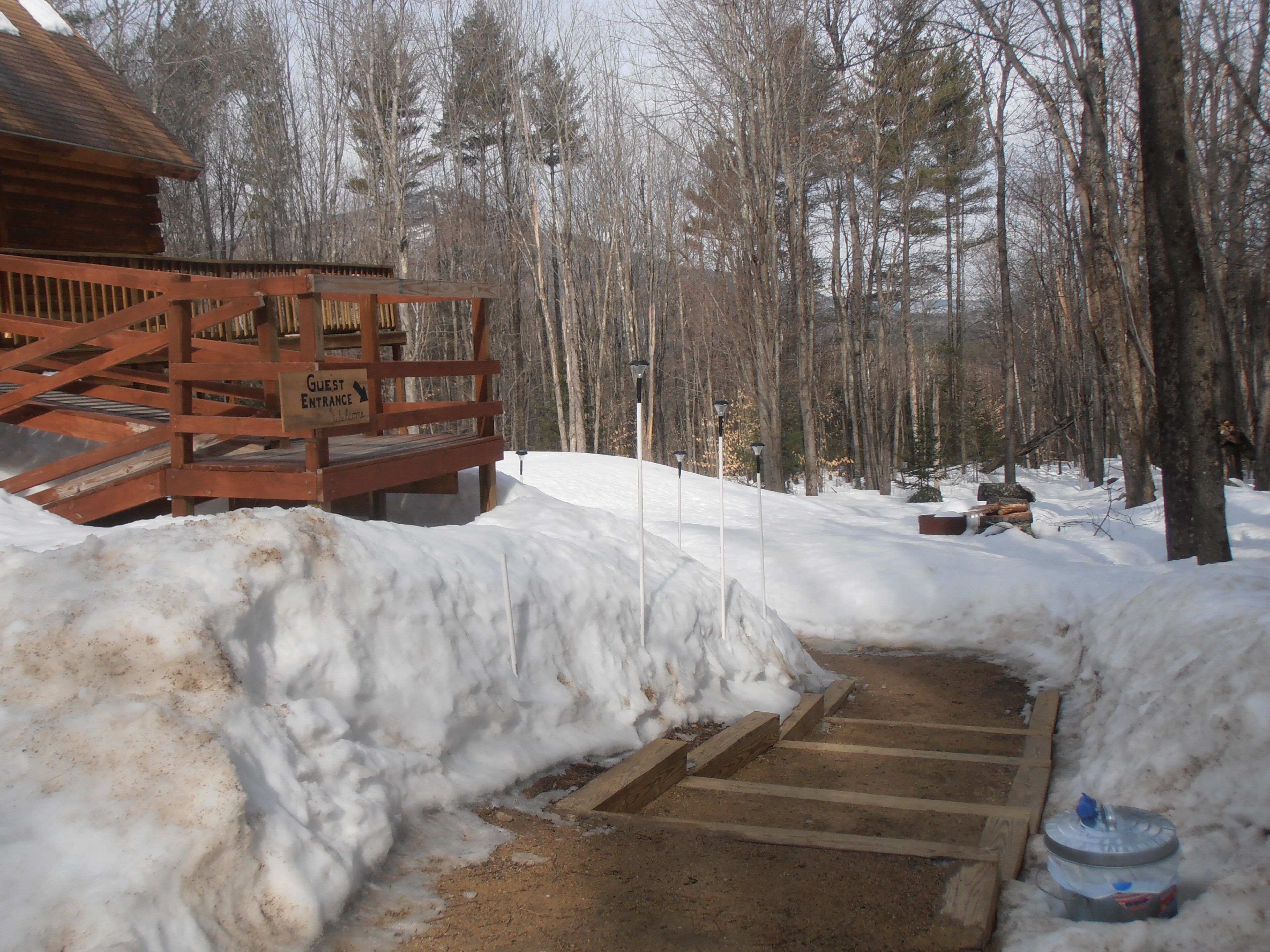 A wooden guest entrance with a snow-covered path leading to a cabin.