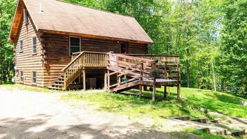A log cabin with a wooden deck and a staircase leading to a porch.