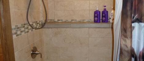 Un bagno con una vasca, un soffione doccia e uno scaffale con articoli da toilette.