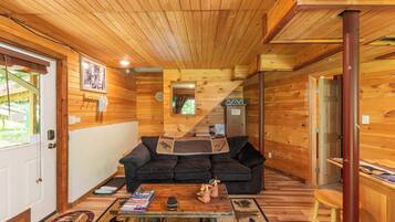 L’intérieur d’un chalet accueillant, avec un plafond en bois, un canapé noir, une table basse et un plancher en bois.