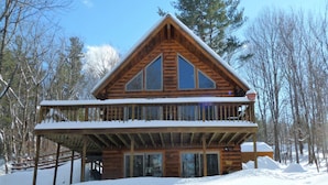 Eine zweistöckige Blockhütte mit Balkon, umgeben von Schnee und Bäumen.