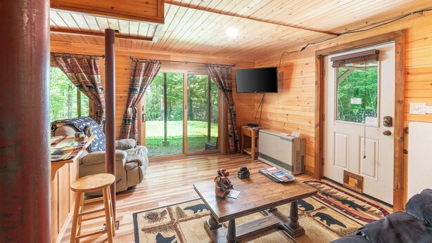 Ein Holzblockhaus-Interieur mit Esstisch, Sofa und an der Wand montiertem Fernseher.