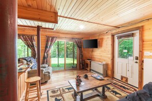 A wooden cabin interior with a dining table, sofa, and a TV mounted on the wall.