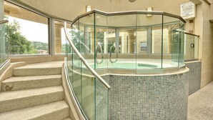 Ein gläsernes Whirlpool-Becken mit Kacheln im Inneren, neben einer Treppe, die zu einer oberen Ebene führt.