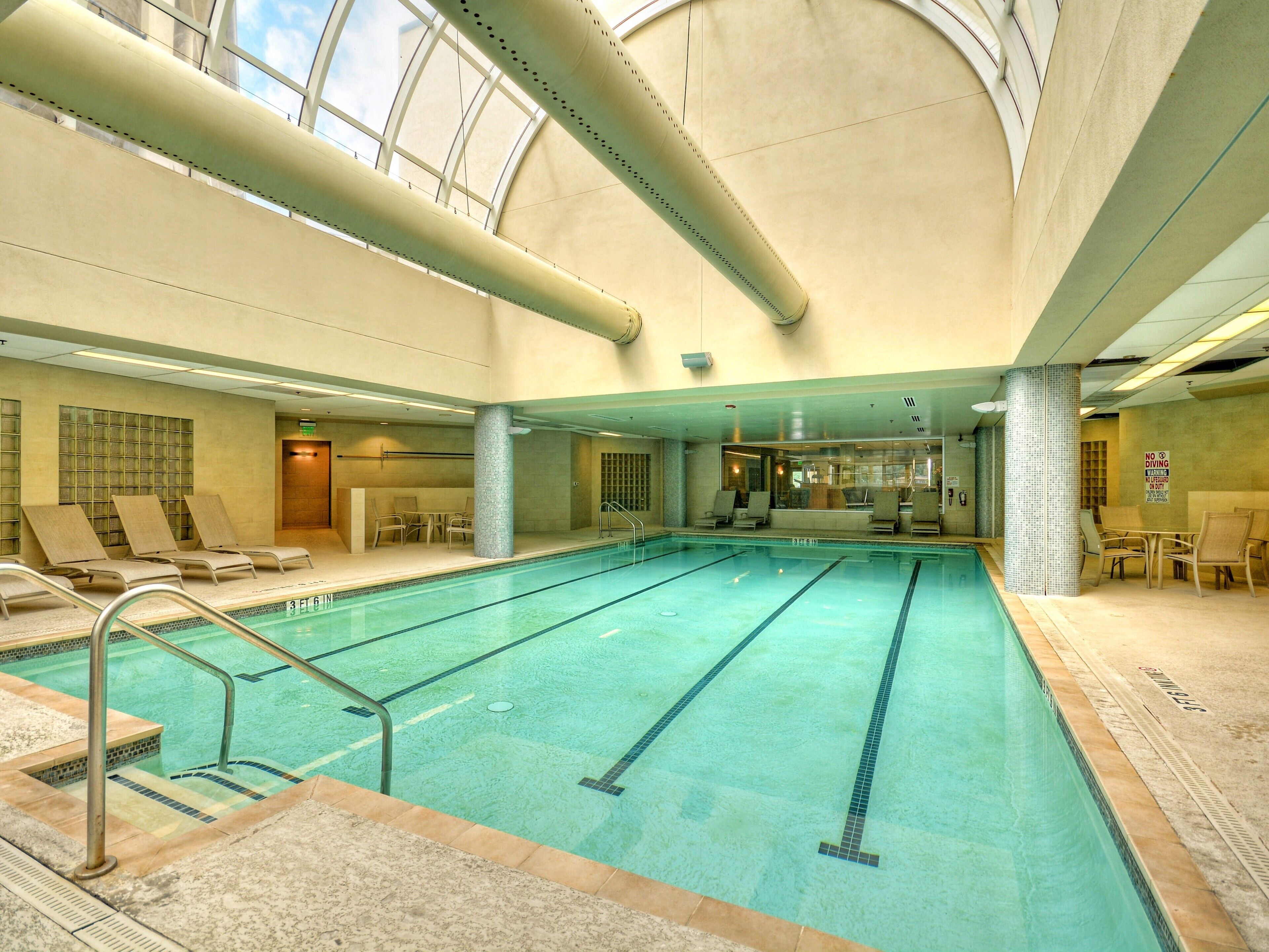 Ein Hallenbad mit markierten Bahnen, Liegestühlen und einer hohen Decke mit Oberlichtern.