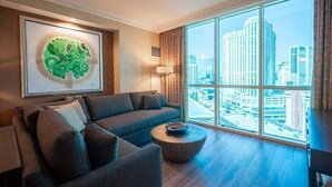 A modern living room with a grey sofa, a round coffee table, and a large window offering a city view.