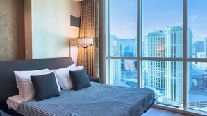A hotel room with a large bed, a city view, and a floor lamp.