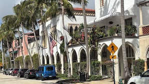 A white building with arched windows and a red-tiled roof, surrounded by palm trees.