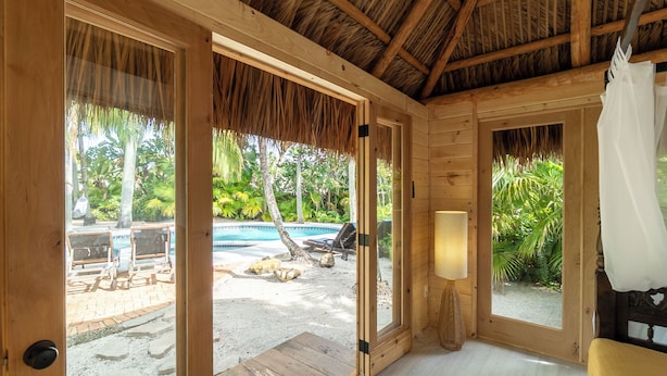 A wooden room with a thatched roof, a pool, and outdoor seating.