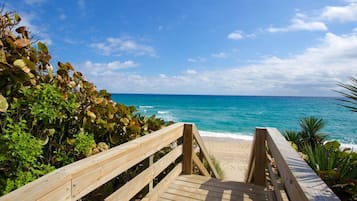 A wooden boardwalk leading to a beach with clear turquoise water and a blue sky.