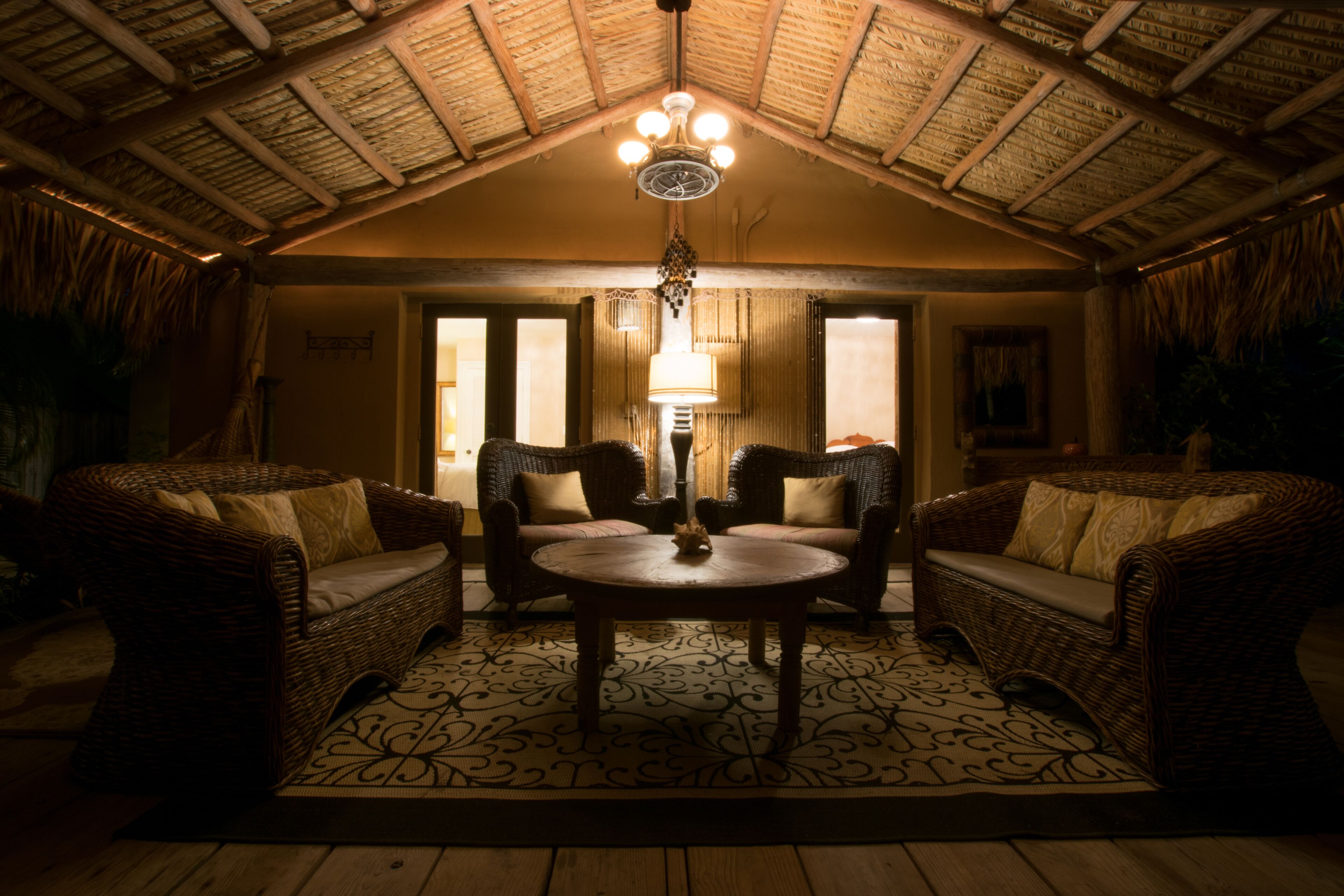 A cozy room with wicker furniture, a round table, and a ceiling with a thatched roof.