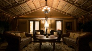 A cozy room with wicker furniture, a round table, and a ceiling with a thatched roof.