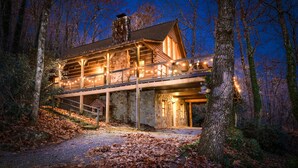 Eine Blockhütte mit Steinunterbau, einer Veranda und einem Steinsschornstein.