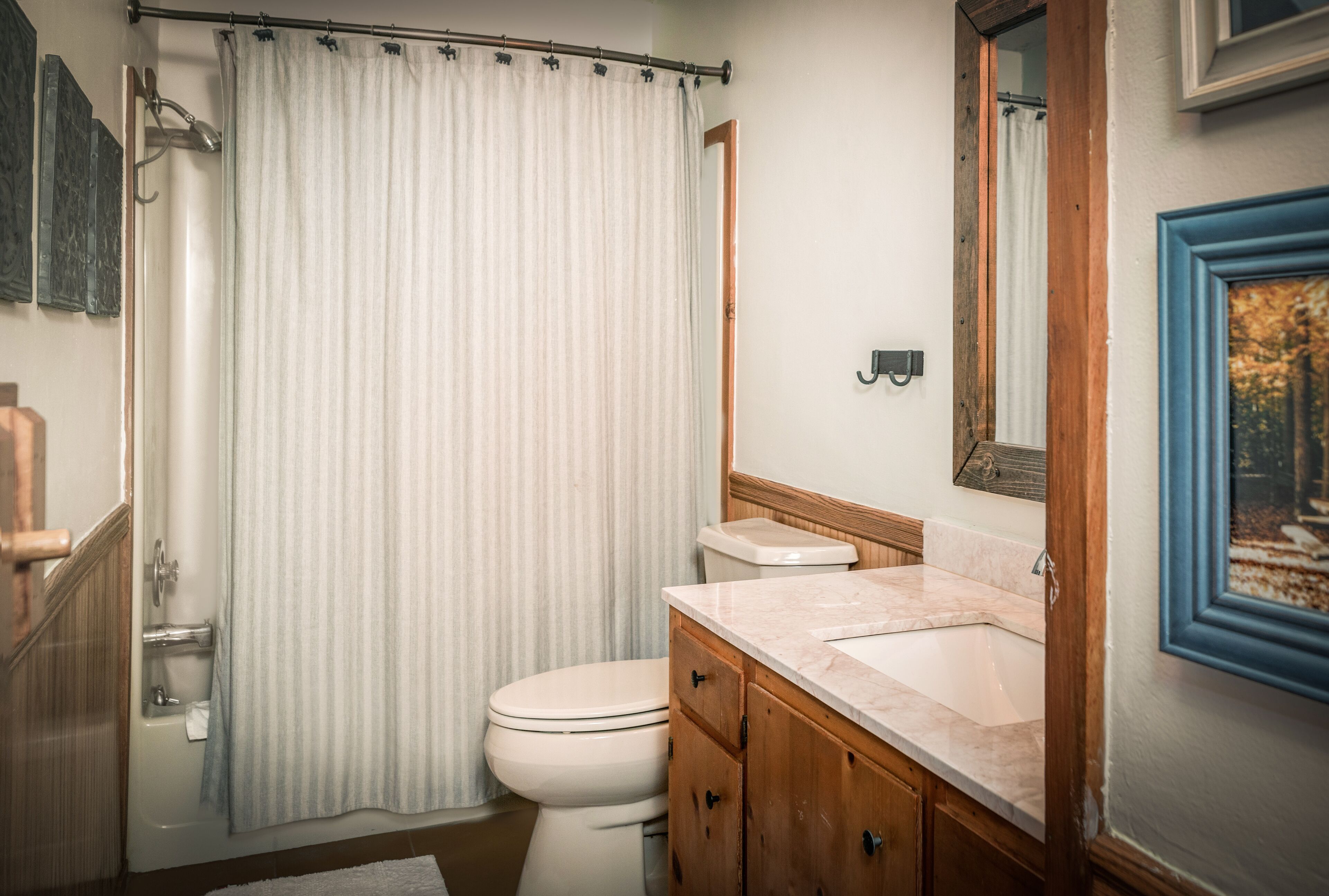 Un baño con cortina de ducha, inodoro, lavamanos y tocador de madera.