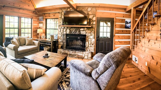Ein gemütliches Blockhaus mit Kamin, Holzwänden, einer Couch und einem Fernseher.