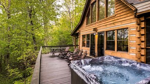 Eine Holzdiele mit Whirlpool und Liegestühlen, umgeben von einem Wald.