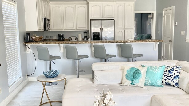 A modern kitchen with white cabinets, a stainless steel refrigerator, and a granite countertop. - BEAUTIFUL 3BR TOWNHOUSE w/ POOL and JACUZZI STEPS FROM BEACH - BOOK NOW! (South Padre Island)