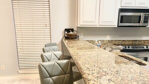A kitchen with a granite countertop, a built-in microwave, and a stainless steel stove. There are three bar stools with cushioned seats. - BEAUTIFUL 3BR TOWNHOUSE w/ POOL and JACUZZI STEPS FROM BEACH - BOOK NOW! (South Padre Island)