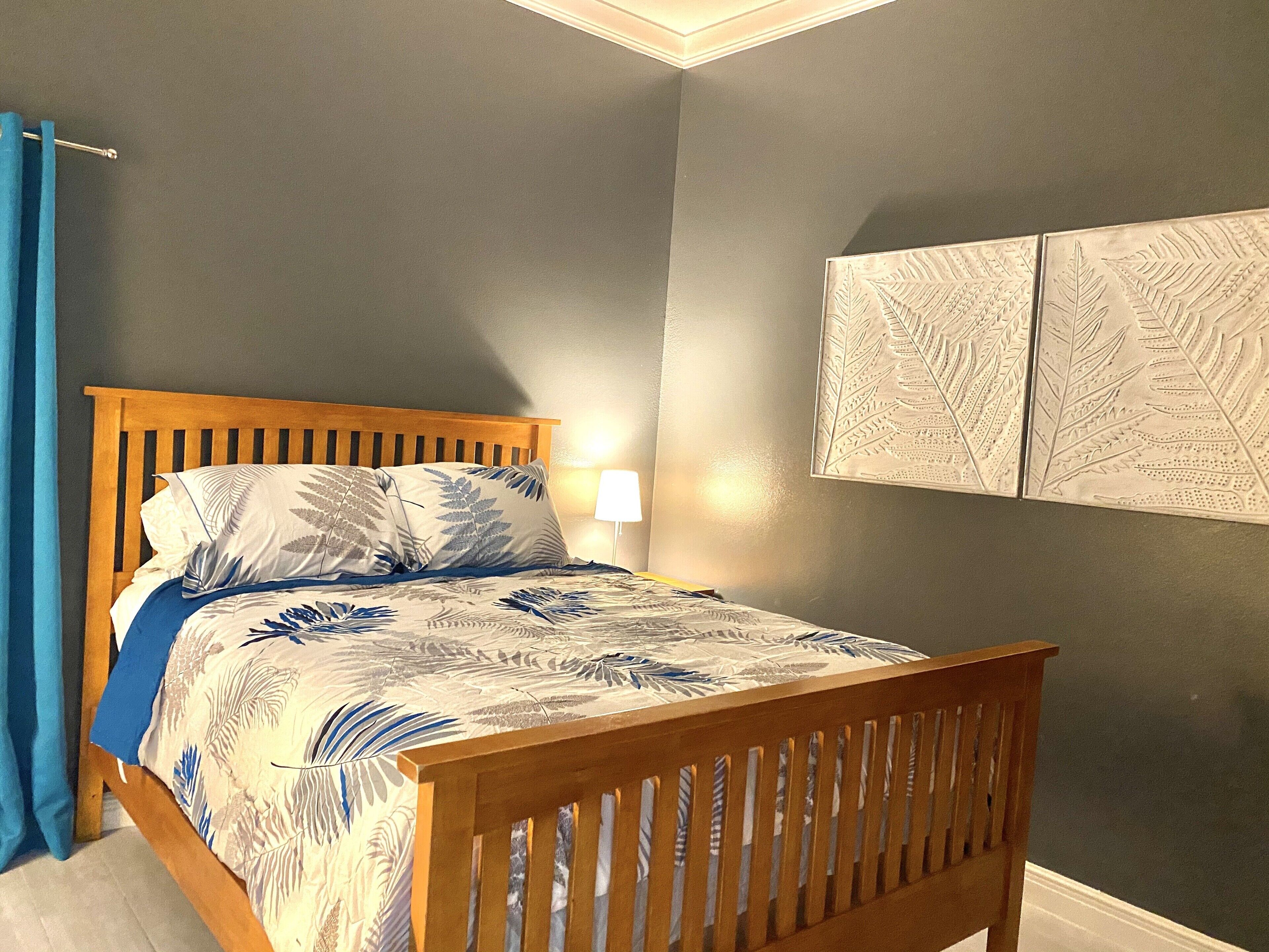 Un dormitorio con cama de madera, cortina azul y lámpara fijada a la pared.