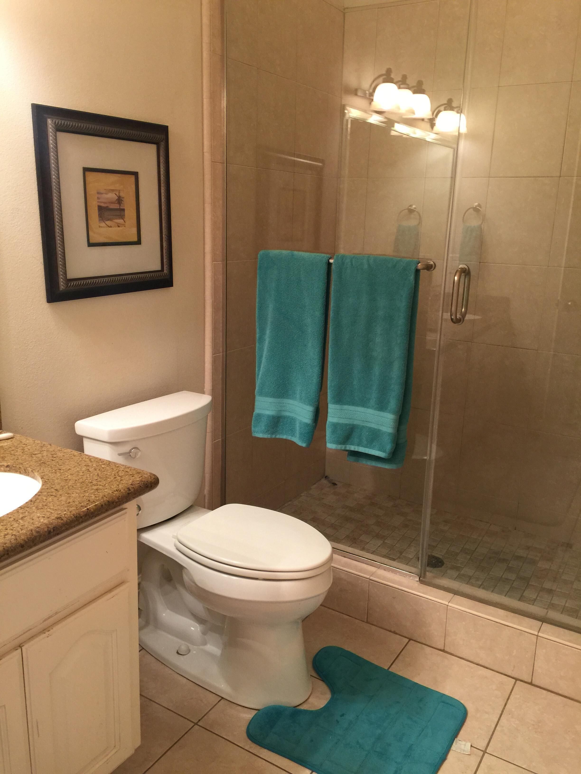 Ein Badezimmer mit Toilette, Waschbecken und Dusche. Zwei Handtücher hängen an der Duschkabinentür.