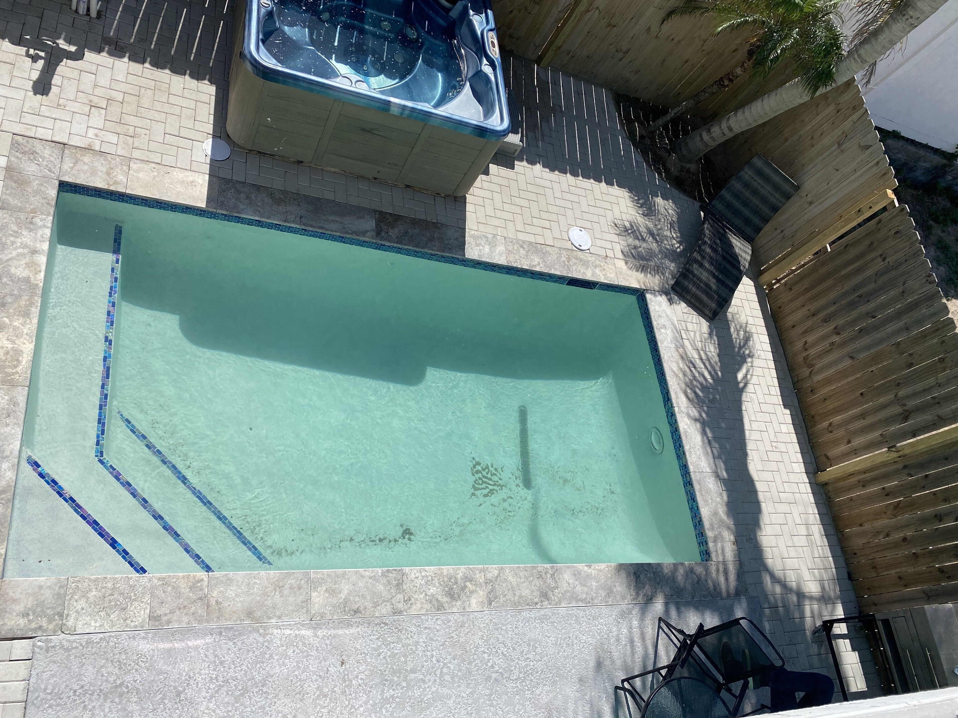 A rectangular swimming pool with a tiled border and a hot tub adjacent to it.