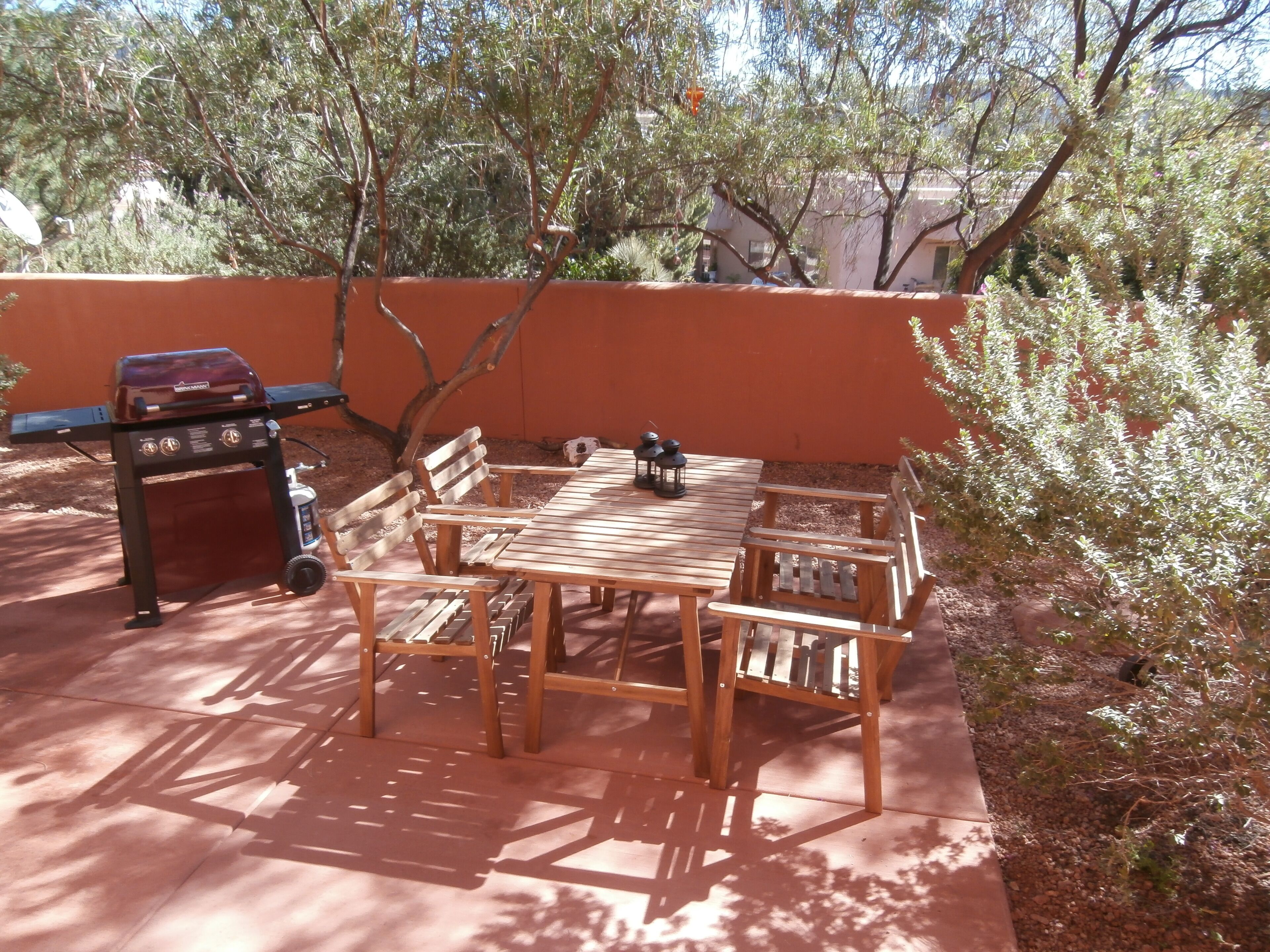 An outdoor patio with a wooden table and benches, a barbecue grill, and a potted plant.