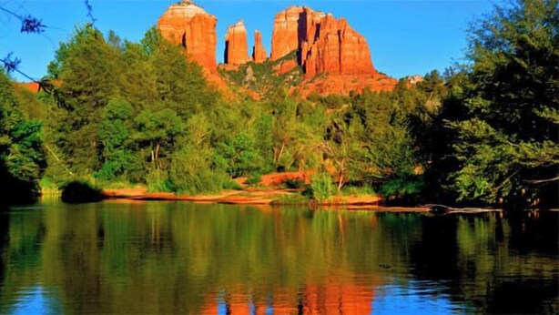 A natural landscape with a calm lake reflecting red rock formations and dense green foliage. - Luxurious, Upscale Townhome In Sedona. Super clean, gourmet kitchen, comfy beds! (Sedona)