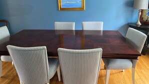 Un comedor con una gran mesa de madera rodeada por seis sillas a rayas, un cuadro en la pared y una lámpara sobre una mesita auxiliar.